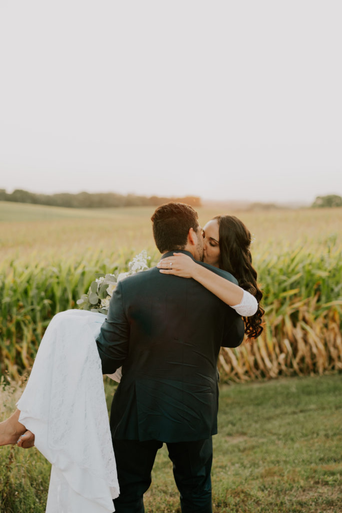 groom holding bride while walking through golden field in Louisville