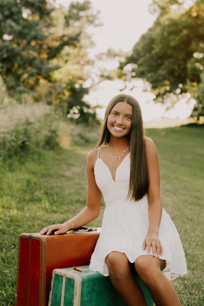 girl sitting on luggage in omaha forest during omaha senior session