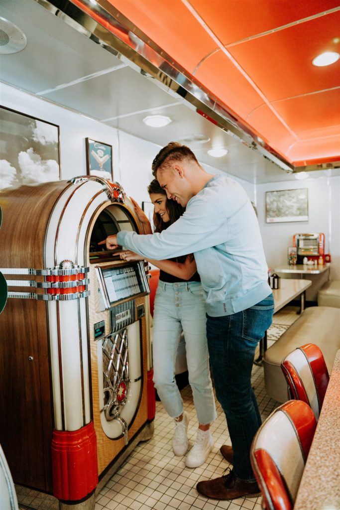 man and woman picking song on jukebox in old school diner making them both feel comfortable in front of camera 