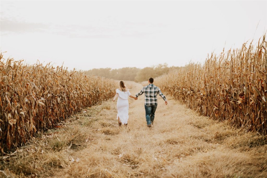 man and woman walking through omaha wheat field getting man comfortable in front of camera