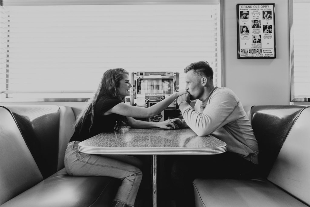 man kissing woman's hand in diner bench