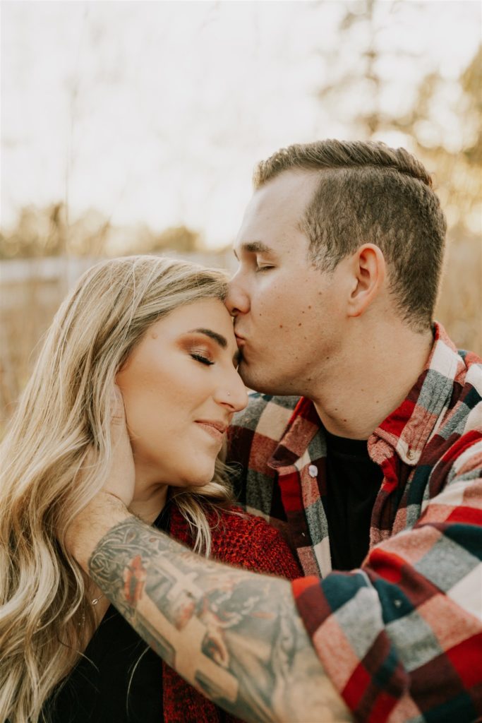man kissing woman on forehead during outdoor engagement session
