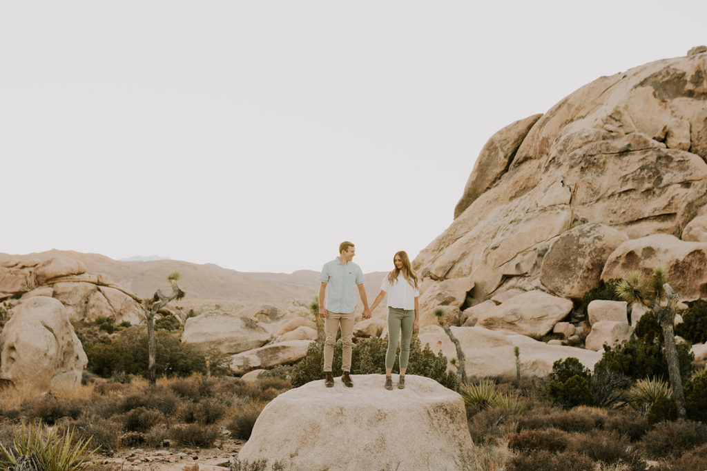 Man and woman holding hands on boulder in Joshua tree