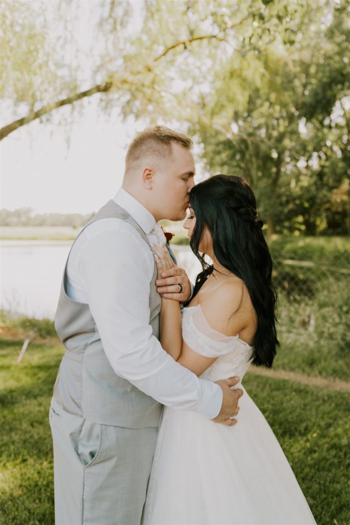 groom kissing bride's forehead during outdoor bridals at backyard wedding