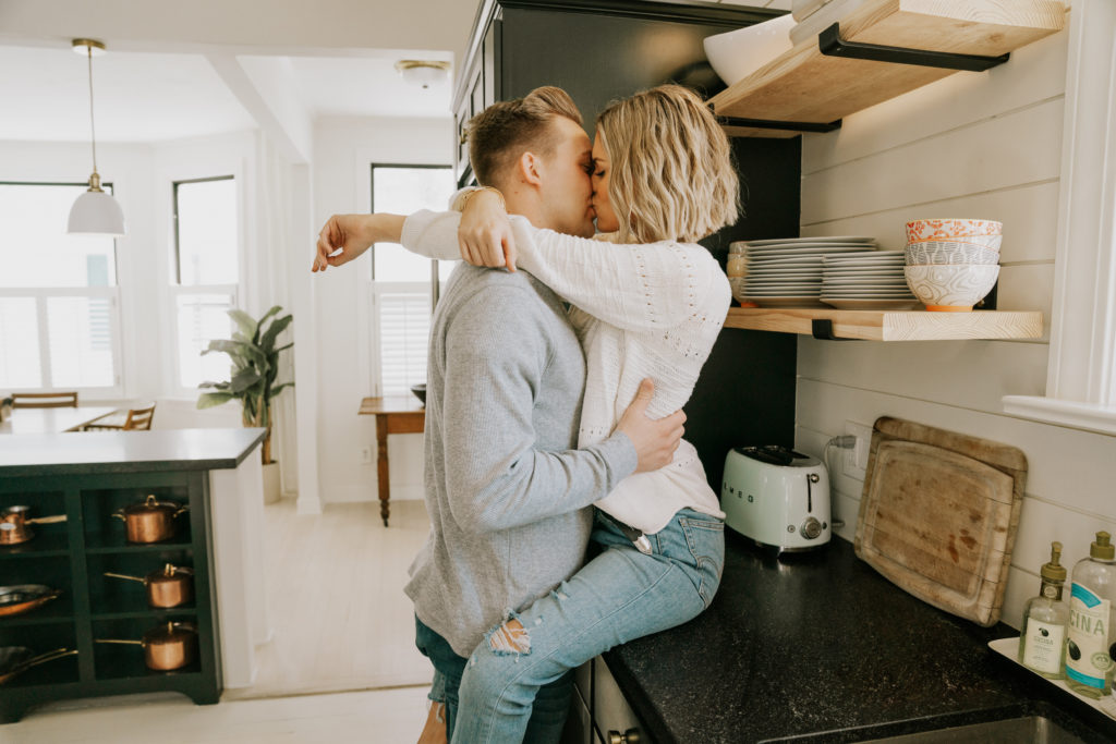 couple posing and kissing during in home engagement session to get more comfortable in front of camera