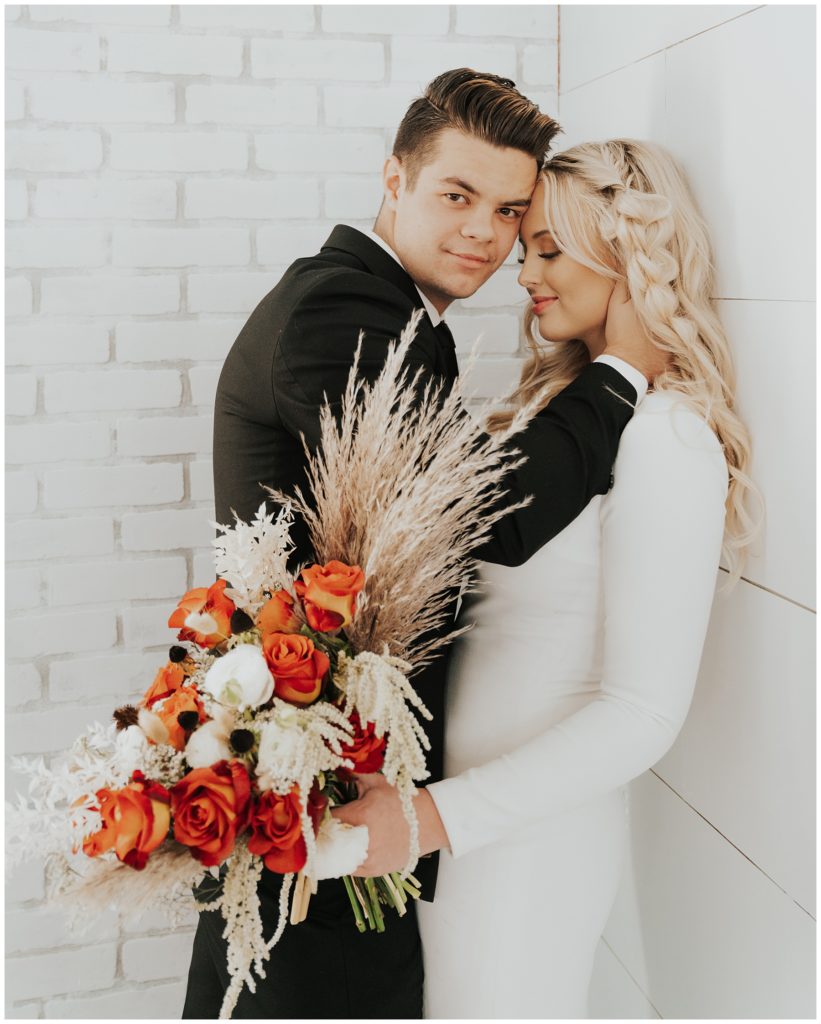 groom pushing bride against wall posing and smiling while the perfect wedding photographer takes their bridals