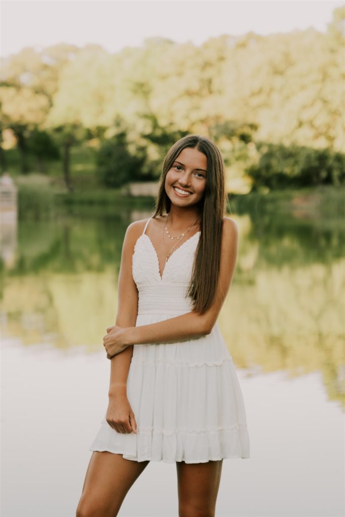 girl holding arm and standing in front of lake during senior sessions in omaha