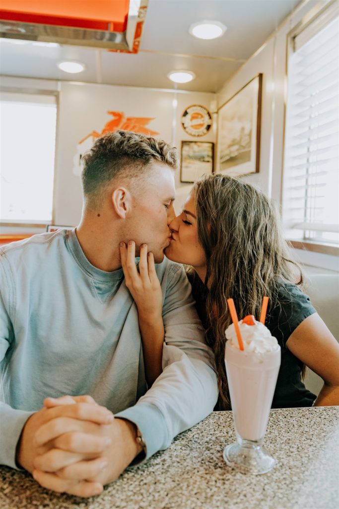 man and woman kissing in diner during engagement session to make them both feel more comfortable in front of camera