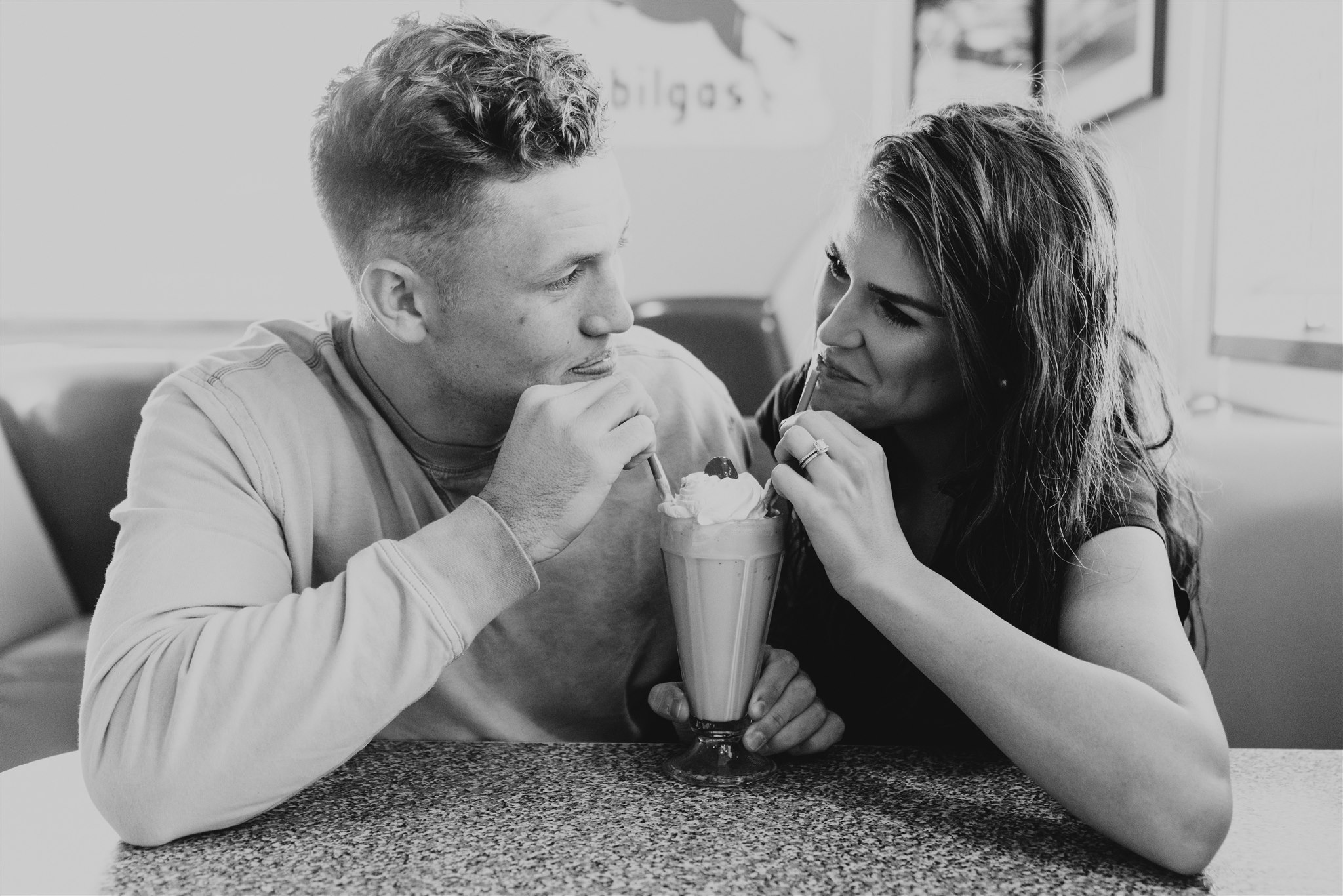 man and woman looking at each other sharing a milkshake during engagement session