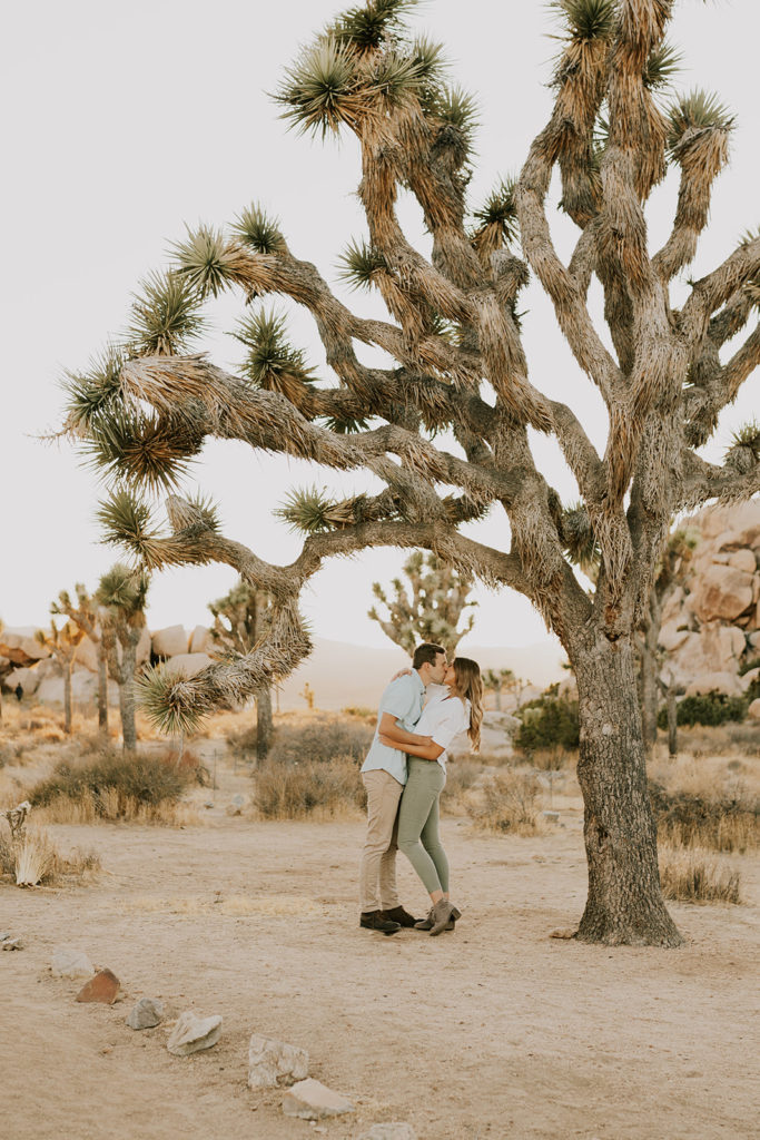 Man and woman hugging and kissing in front of Joshua Tree couple session