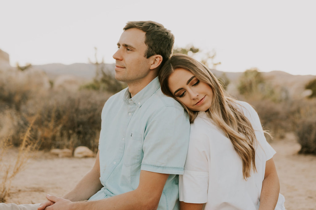 Man and woman sitting together with woman resting head on man’s shoulder in Joshua tree couple session