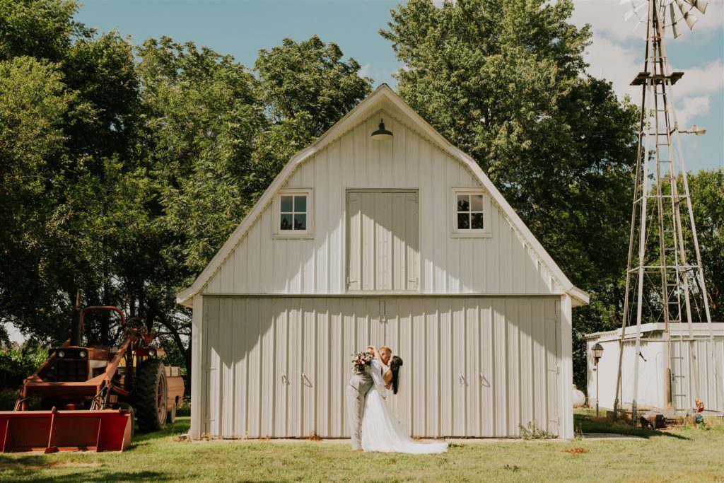 bride and groom kissing in front of barn at wedding