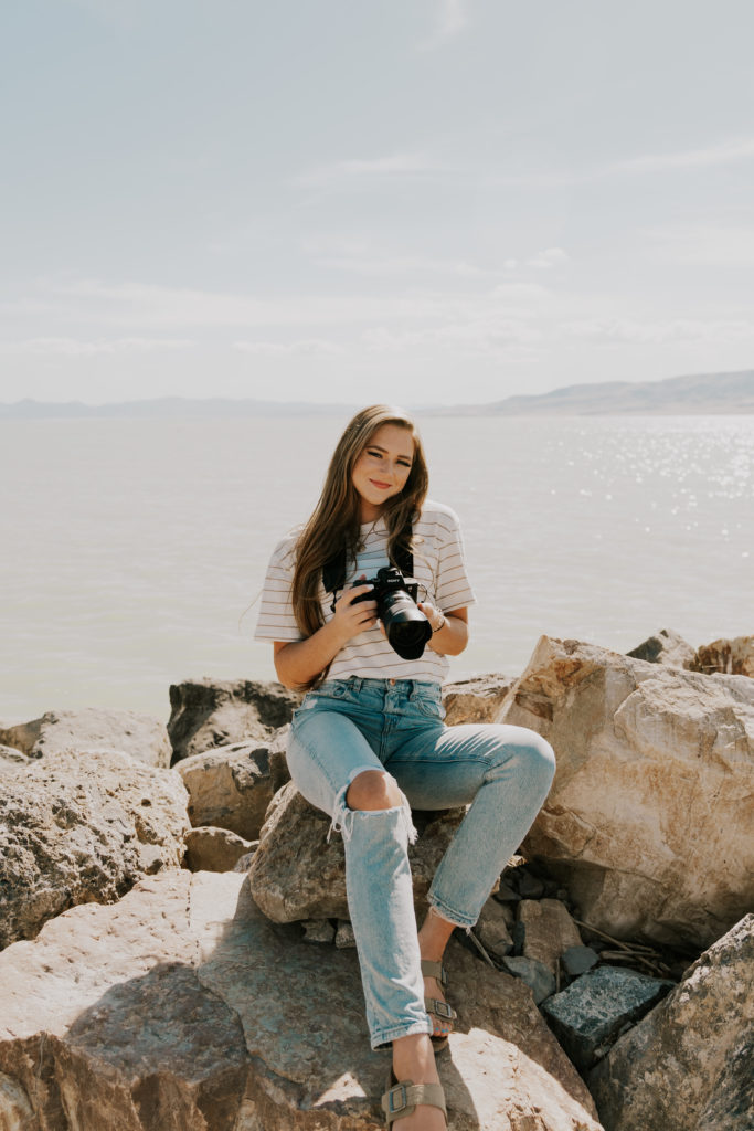 photographer holding her camera sitting on a rock on the beach beside the California ocean